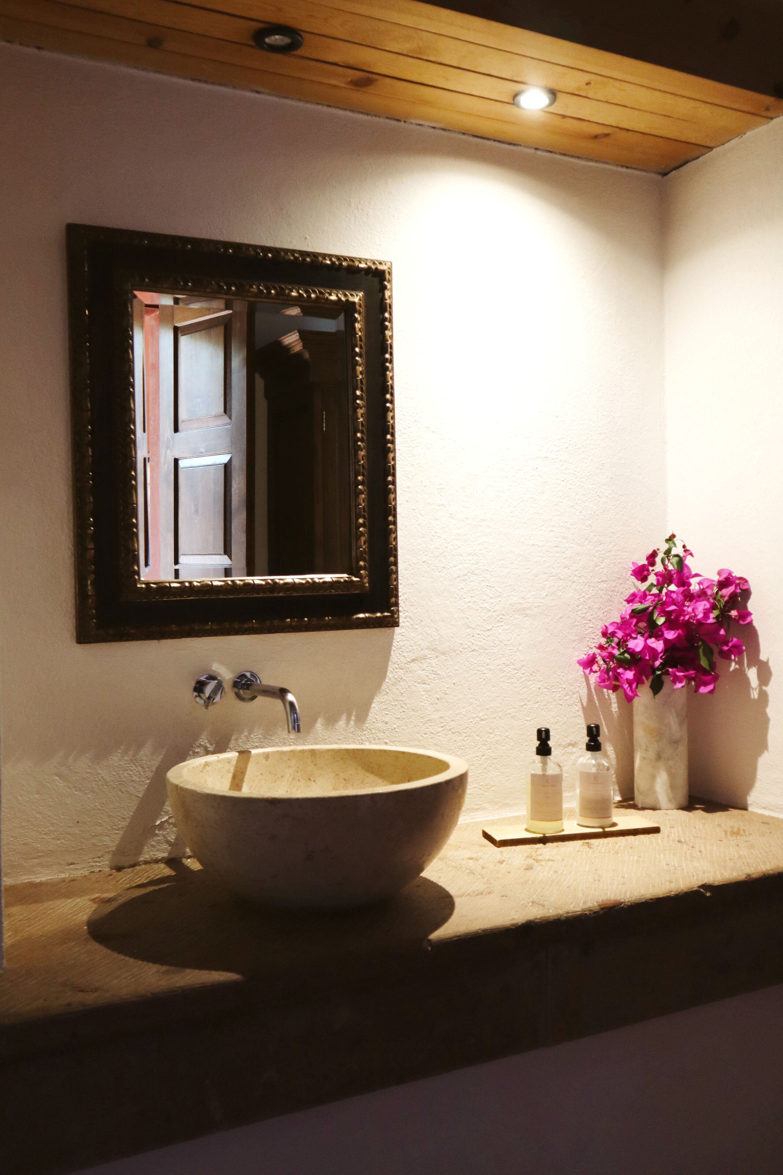 A bathroom with a large mirror, a sink, and a vase with flowers.