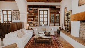Una sala de estar acogedora con un sofá blanco, una mesa de centro y una alfombra estampada. Se ven estanterías llenas de libros y una chimenea.