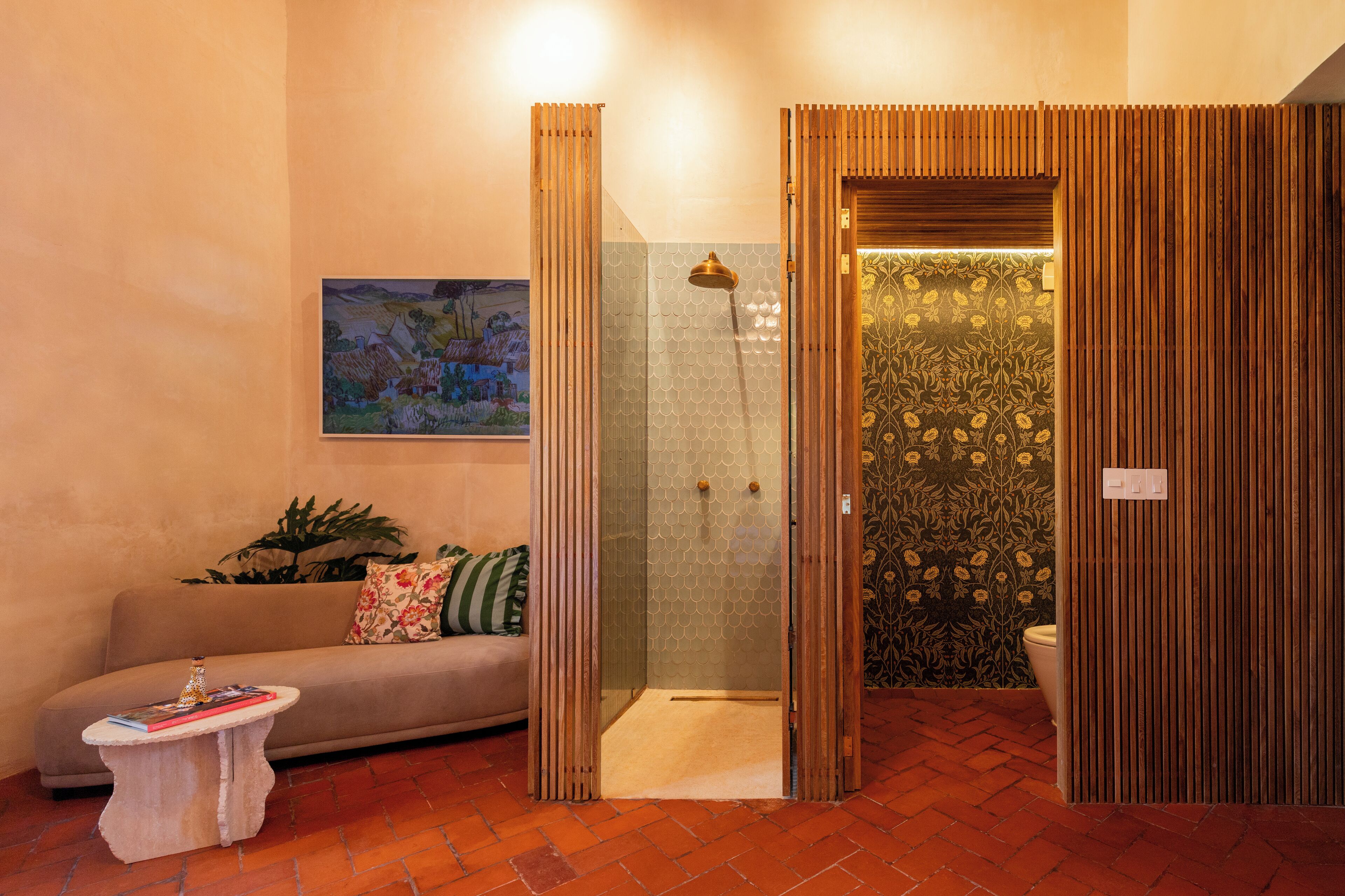 A bathroom with a shower, a toilet, and a sink. There is a sofa and a small table with a book and a bottle.