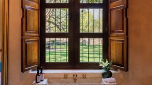 Un baño con tocador de madera, un lavamanos y una ventana con contraventanas abiertas.