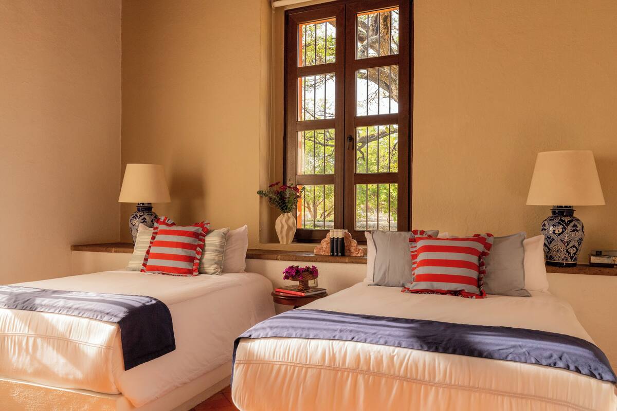 A hotel room with two beds, each with a pillow and a bedside table with a lamp.
