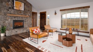 A modern living room with a stone fireplace, leather sofas, a coffee table, and a large window offering a view of the mountains. - A 160 Acre Luxury Modern Ranch (Belgrade)