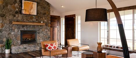 A spacious living room with a stone fireplace, leather sofas, a large window, and a modern pendant light.