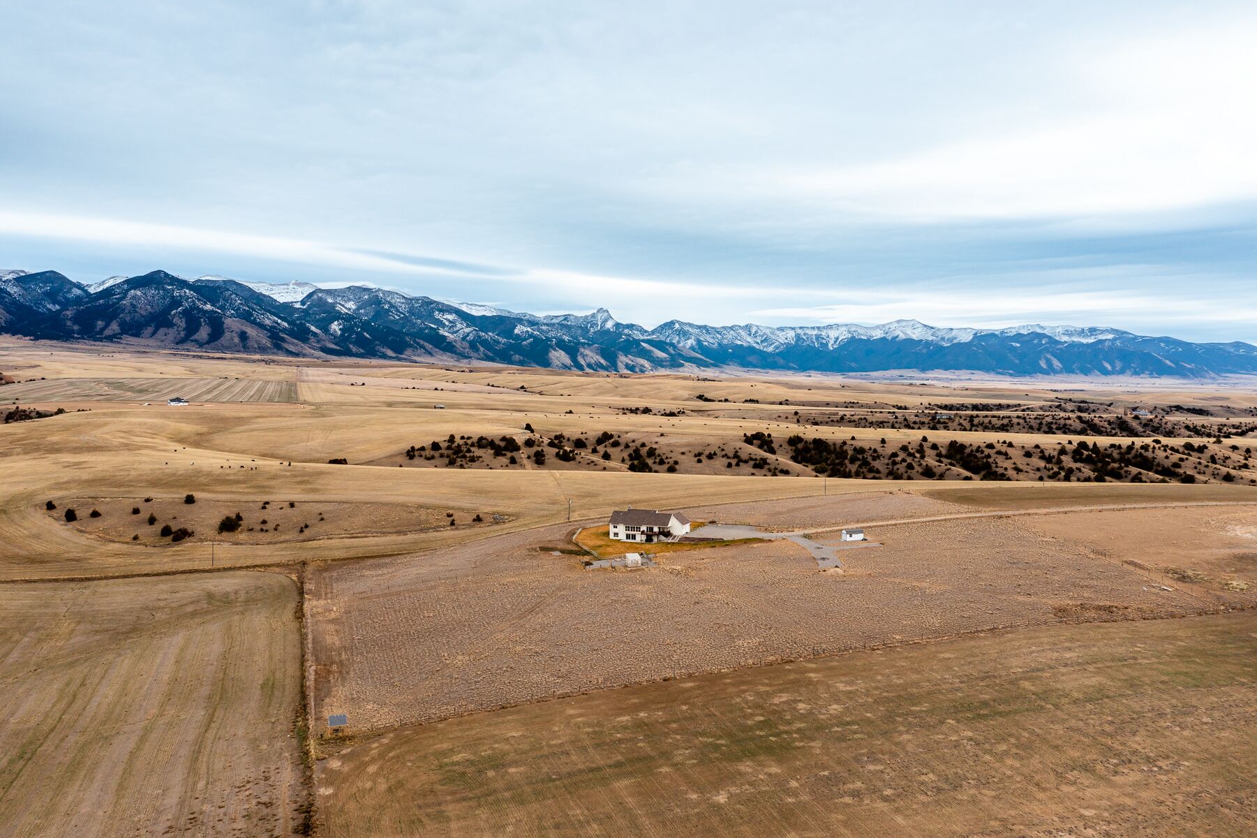 Une vue aérienne d’un paysage rural, avec une maison entourée de champs et des montagnes en arrière-plan.