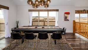 A dining area with a large table, black chairs, a woven rug, and a view of the landscape through large windows. - A 160 Acre Luxury Modern Ranch (Belgrade)