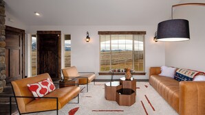 A modern living room with a stone wall, leather furniture, a large window with a view of mountains, and a wooden door. - A 160 Acre Luxury Modern Ranch (Belgrade)