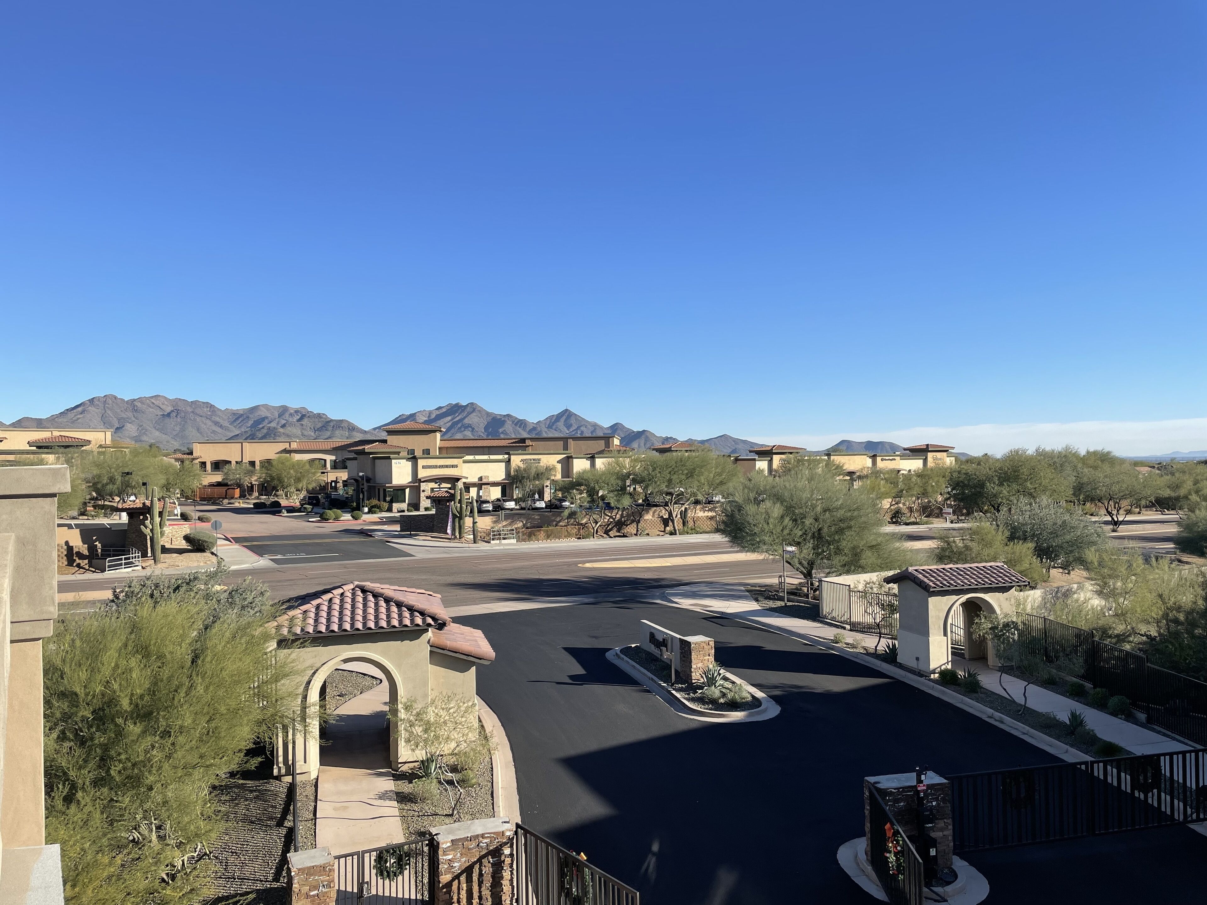 A parking lot with a central island, surrounded by buildings with arched entrances and a mountain backdrop.