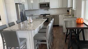 Een moderne keuken met witte kasten, een centraal eiland met zitplaatsen, en een eethoek met een decoratieve pompoen.