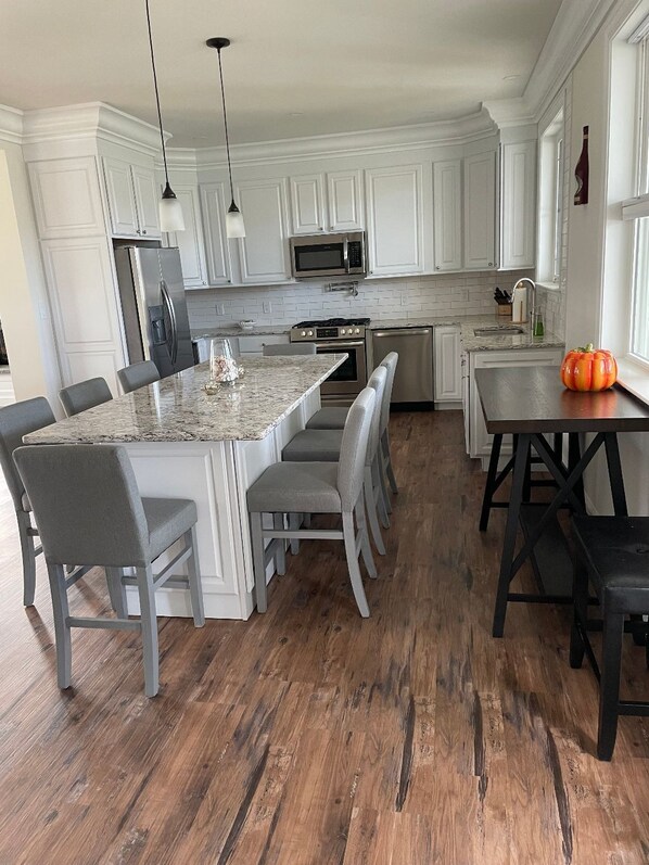 A modern kitchen with white cabinetry, a central island with seating, and a dining area with a pumpkin centerpiece.