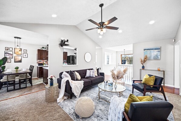 A spacious living room with a dark-colored sofa, a round coffee table, and a ceiling fan.
