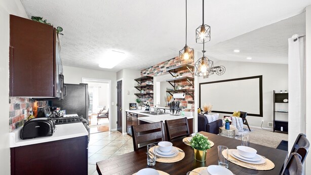 Une cuisine moderne dotée d’une cuisinière intégrée, de meubles de rangement aux couleurs sombres et d’un mur d’accent en briques.