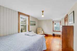 A bedroom with a bed, a chair, a dresser, and a window. - Joppa Flat (Newburyport)