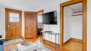 Uma sala de estar moderna com uma porta de madeira, uma TV de tela plana presa a um suporte de metal, uma mesa de centro branca e um sofá azul.