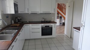 Een keuken met witte kastjes, een roestvrijstalen spoelbak, een koffiezetapparaat en een klok aan de muur.