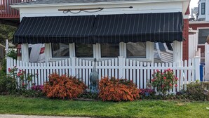 Ein Haus mit schwarzem Markisenvorbau, weißem Zaun und orangefarbenen Blumen im Vorgarten.