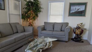 Ein Wohnzimmer mit zwei grauen Sofas, einem Glastisch mit Holzfuß und einer Blumentopf mit Lichterkette sowie einem gerahmten Bild an der Wand.