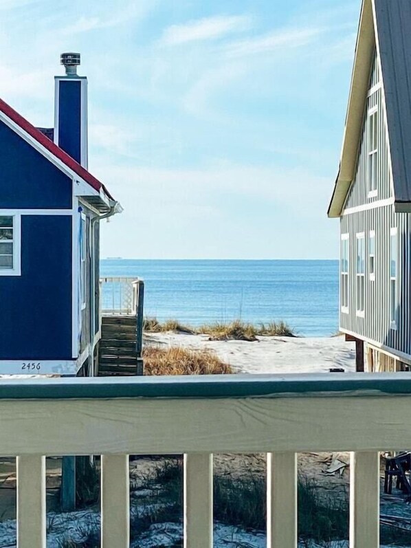 A beachfront property with a blue house and a white house, both featuring a balcony and a view of the ocean.