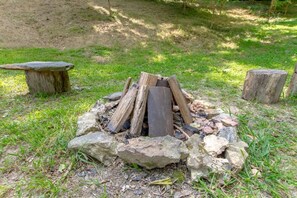 Relax by the fire pit surrounded by trees and grassy area.