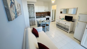 Een ruimtelijke leefruimte met een kitchenette, een eethoek en een bank met rode kussens.