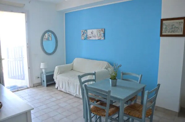 Una habitación con un sofá blanco, una mesa de comedor con sillas, una pared azul y una pequeña planta en maceta.