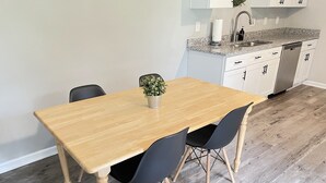 A dining area with a wooden table and black chairs, a potted plant, and a kitchen in the background. - Spacious 4 bedroom home near Charleston & beaches! (Ladson)