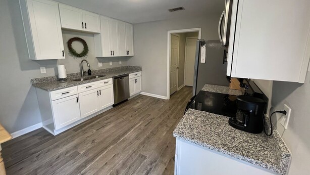 A modern kitchen with white cabinets, a stainless steel dishwasher, and a granite countertop. - Spacious 4 bedroom home near Charleston & beaches! (Ladson)