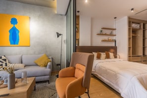 Relax in this stylish bedroom with a large bed, sofa, and armchair, surrounded by a beautiful abstract painting and shelving.
