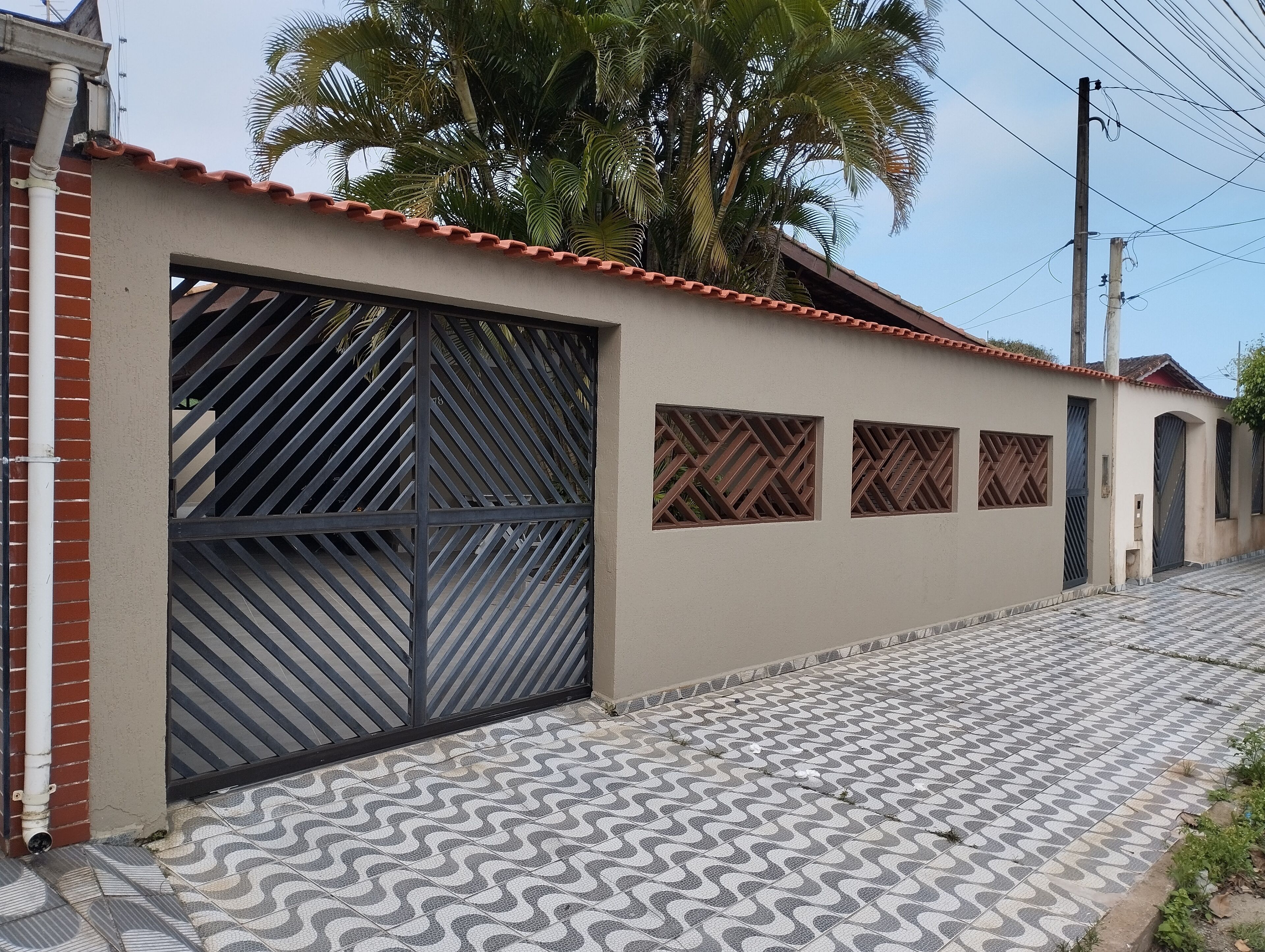 A residential building with a tiled entrance, a metal gate, and a palm tree in the background.