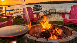A fire pit with chairs around it, overlooking a body of water with a sunset. - Lakeside, New Large Dock & Mooring Ball. On beautiful  Lake Charlevoix 🥂 (East Jordan)