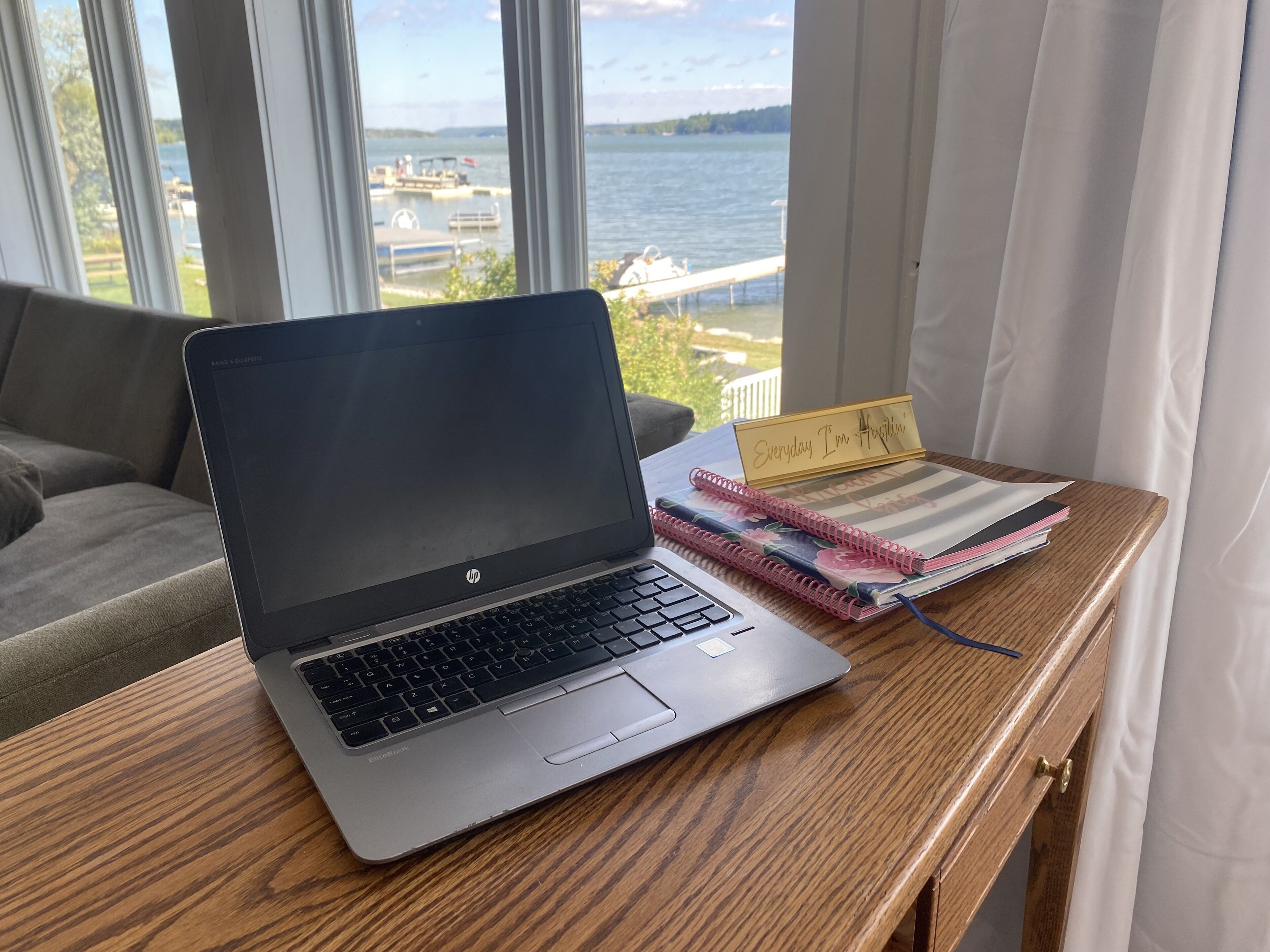 Um laptop sobre uma mesa de madeira com um caderno e uma placa que diz 'Everyday I'm Hustlin'.