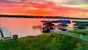 A lakeside dock with boats, a grassy area, and a white fence. - Lakeside, New Large Dock & Mooring Ball. On beautiful  Lake Charlevoix 🥂 (East Jordan)