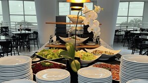 A buffet setup with various dishes, a large window, and a modern interior. - Favorita Golden Hotel e Eventos (Sao Jose)