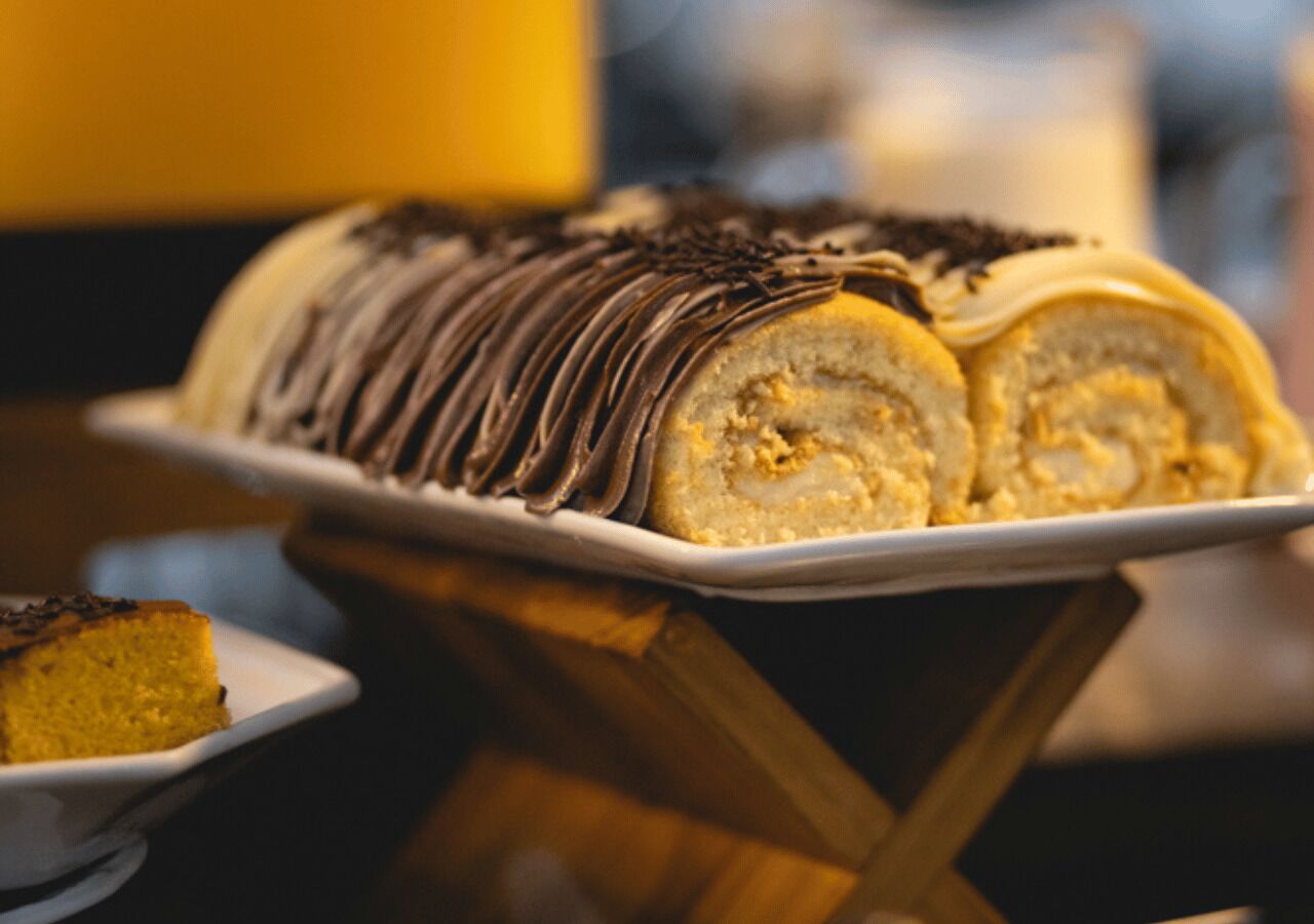 Una bandeja de postres con un rollo bañado en chocolate y una porción de pastel sobre un plato blanco.