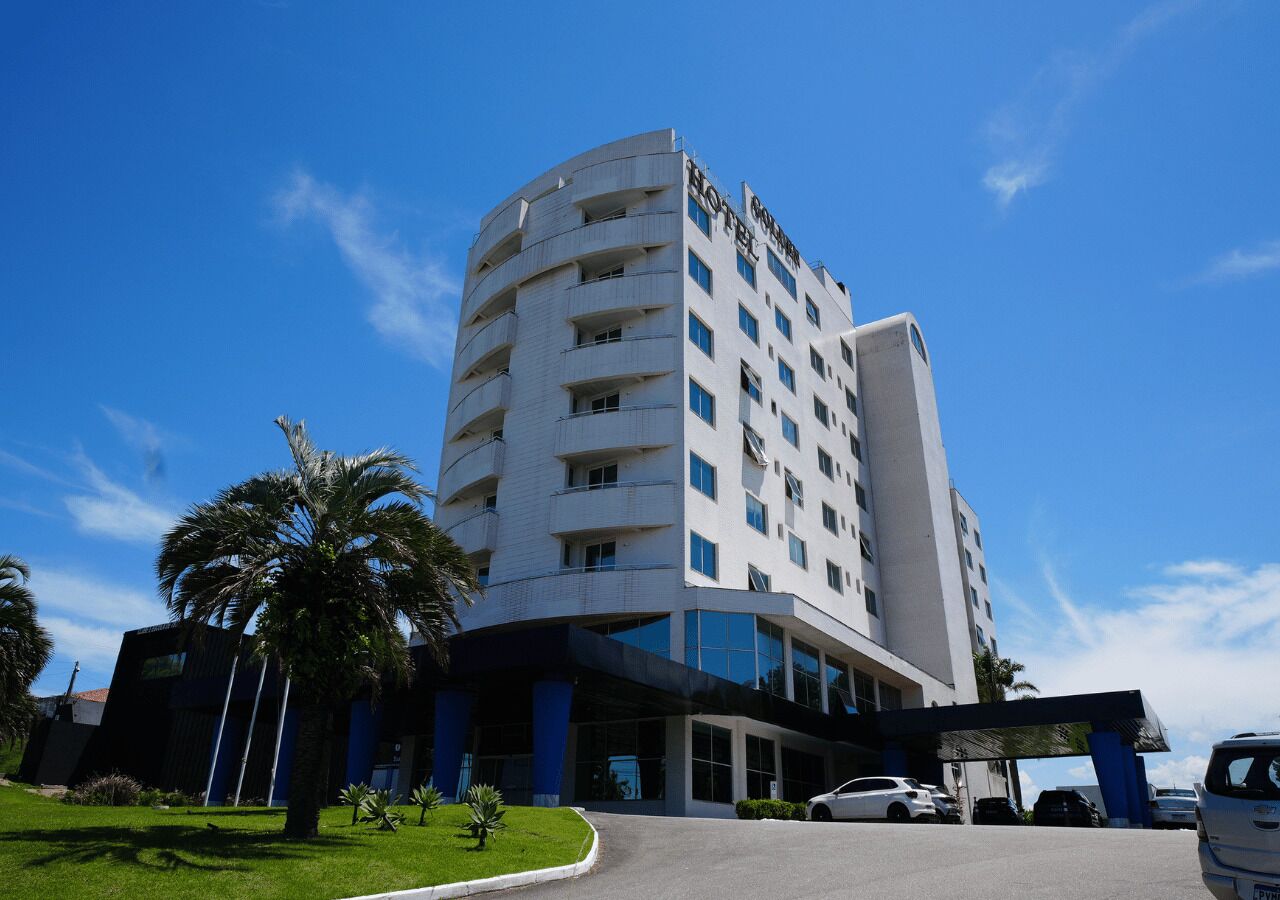 A multi-story hotel with a curved facade, a covered entrance, and a parking area.