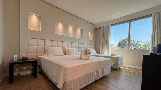 A modern bedroom with a large bed, bedside tables, and a view of the outdoors. - Favorita Golden Hotel e Eventos (Sao Jose)