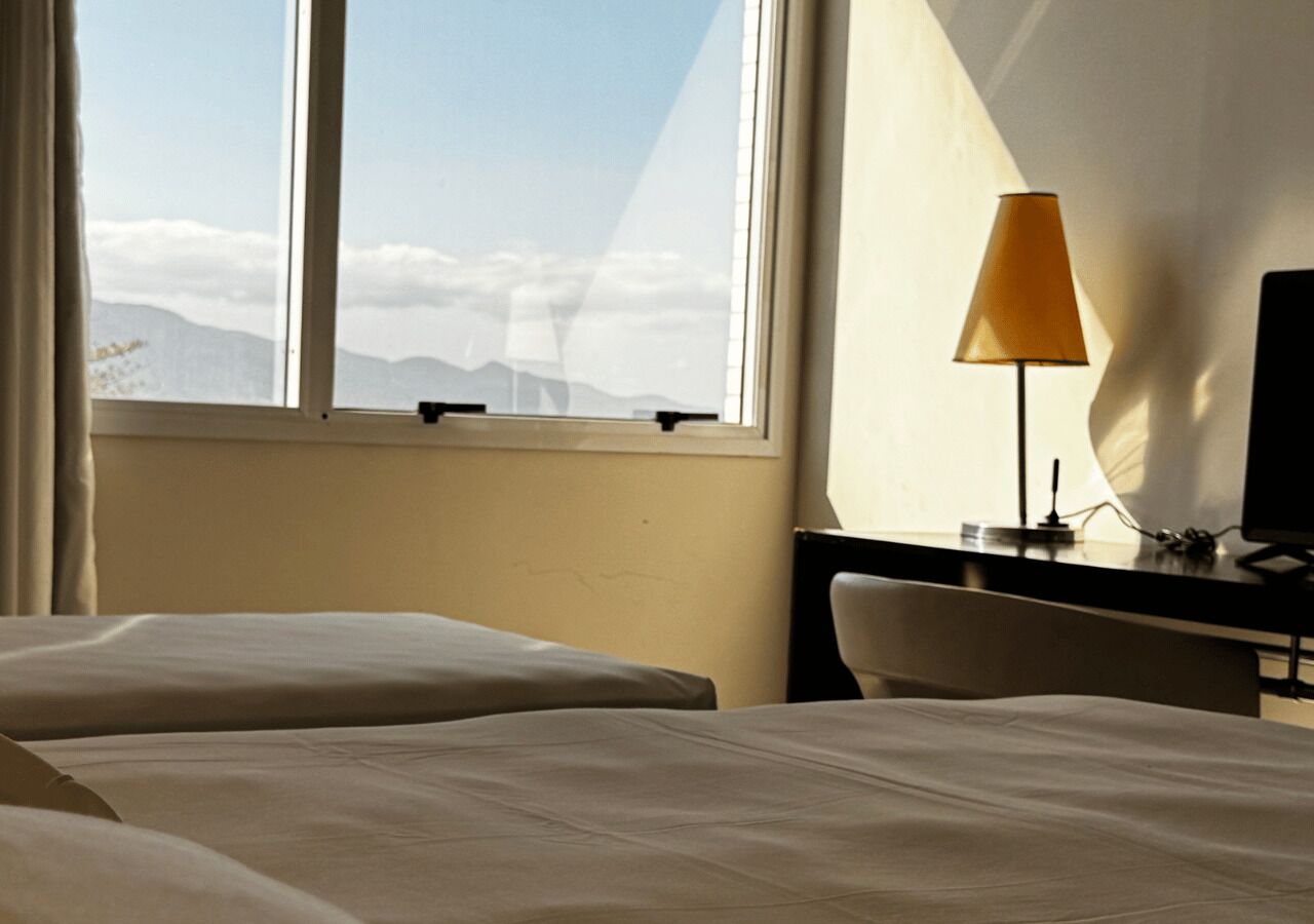 A hotel room with a bed, a desk, a lamp, and a view of mountains through the window.