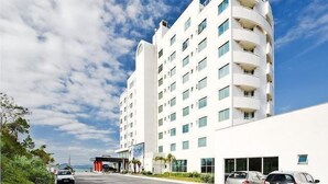 A multi-story hotel with a white facade, balconies on each floor, and a parking area in front. - Favorita Golden Hotel e Eventos (Sao Jose)