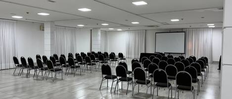 Un salón de conferencias con filas de sillas, una pantalla de proyector y una pizarra.