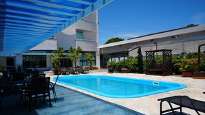 A swimming pool with lounge chairs and a pergola, surrounded by potted plants and a modern building. - Favorita Golden Hotel e Eventos (Sao Jose)
