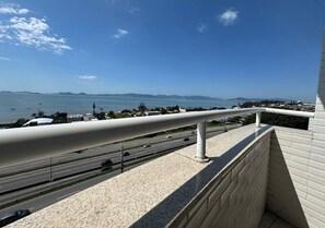 A balcony with a view of a coastal road, a bridge, and distant mountains.