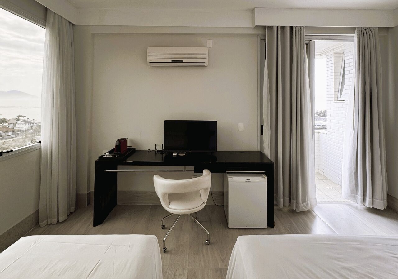 Habitación de hotel con cama, escritorio, silla, refrigerador pequeño y aire acondicionado.