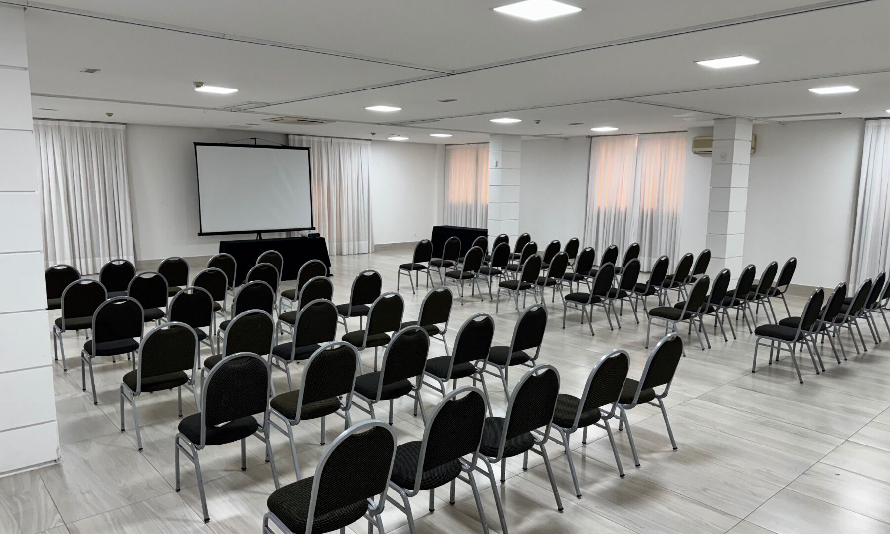 A conference room with rows of chairs, a projector screen, and a large window with curtains.