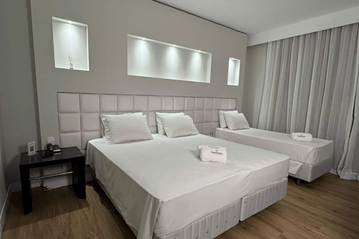 Ett hotellrum med en stor säng, en mindre säng, ett sängbord och en spegel.