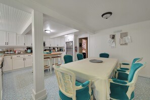 A kitchen with white cabinets, a dining table with teal chairs, and a refrigerator.