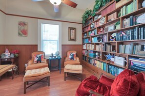 A cozy reading nook with two armchairs, a wooden bookshelf filled with books, and a small table with a globe and flowers.