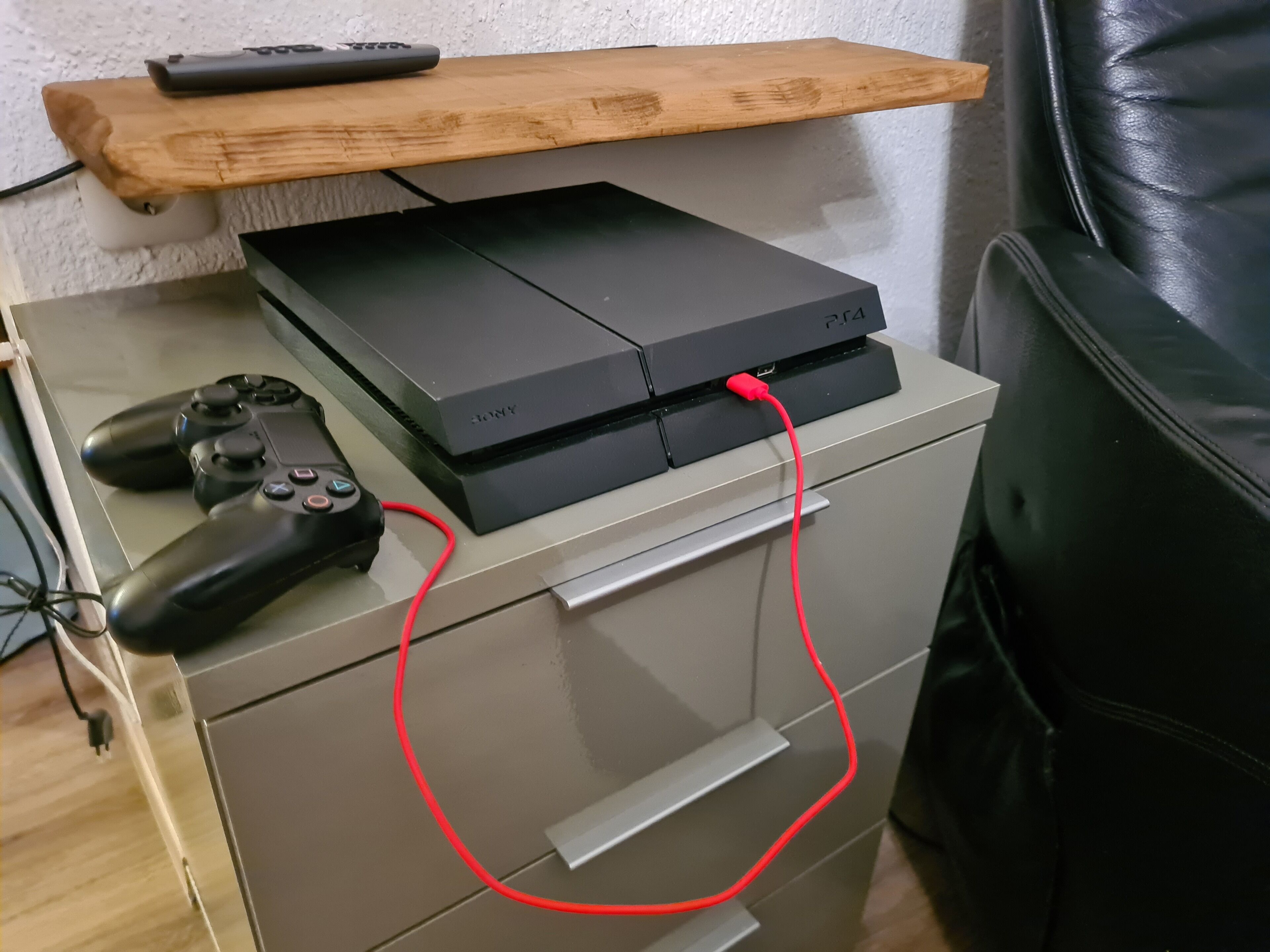 A PlayStation 4 console connected to a controller, placed on a cabinet with drawers.
