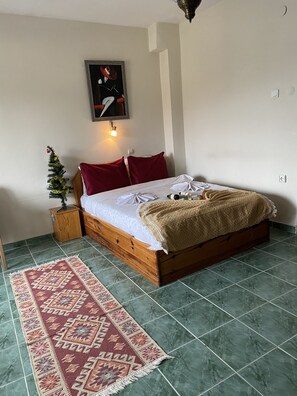 A neatly made bed with a red and white blanket, a small wooden nightstand with a plant, a red pillow, and a framed picture on the wall. - Can Termal & Kaplica Apart Hotel (Termal)