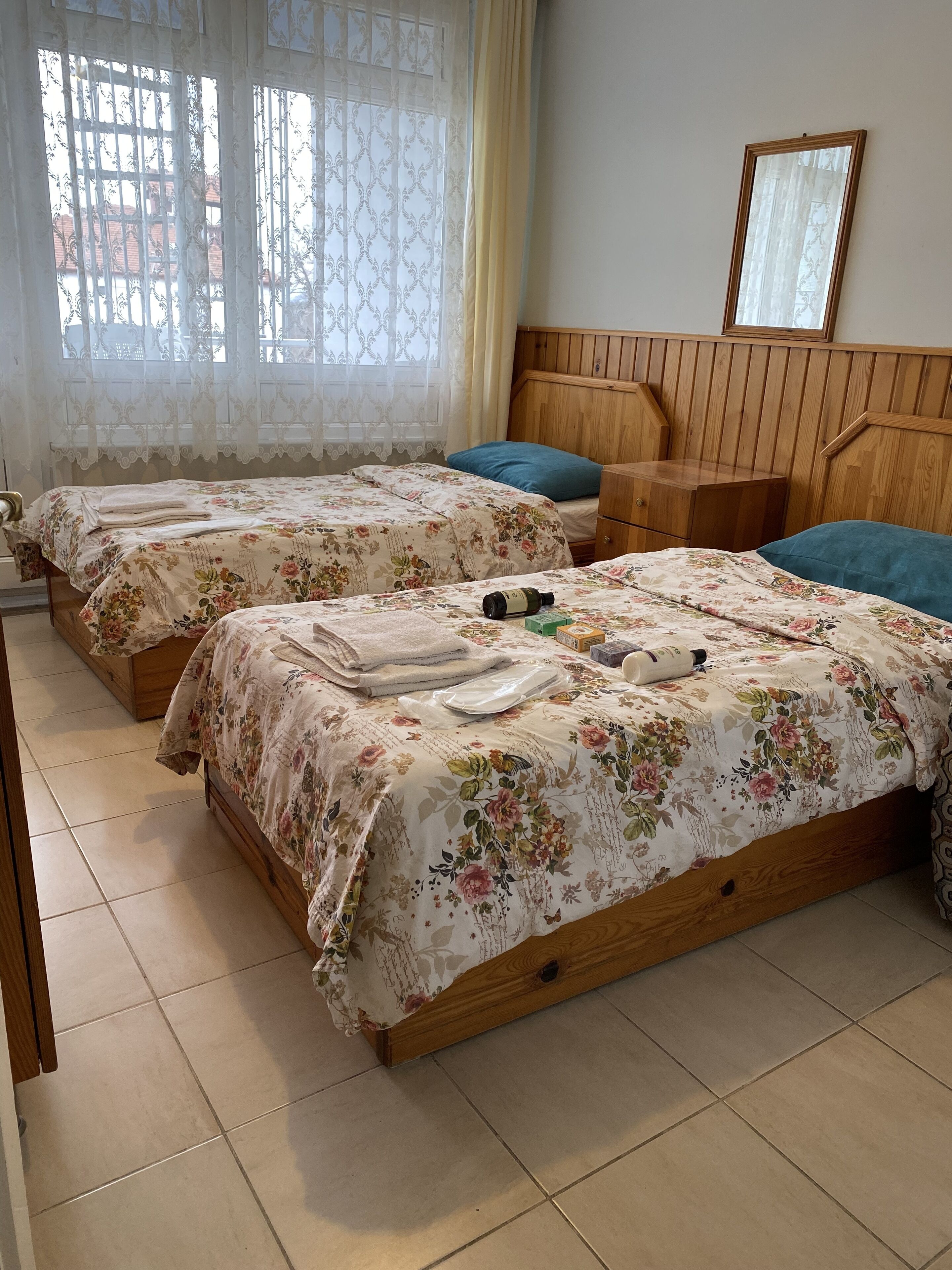A room with two wooden beds, each with floral bedding and blue pillows. There is a wooden nightstand with a mirror above the bed on the right.