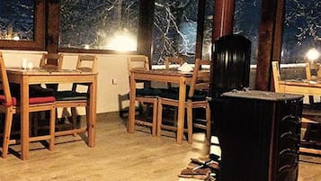 A room with a dining table and chairs, a fireplace, and a view of trees through large windows.