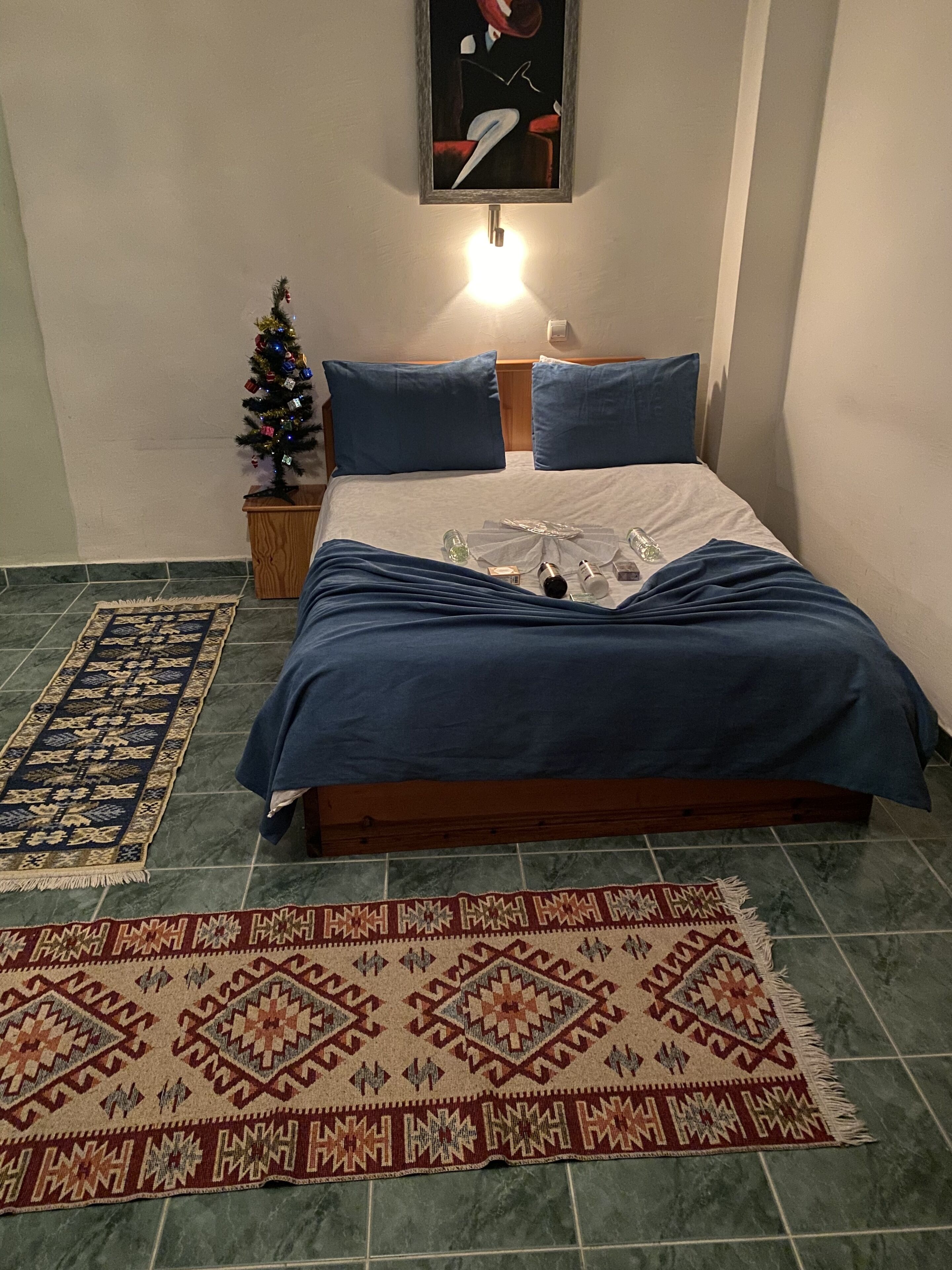 Um quarto bem arrumado com uma cama, uma mesinha de cabeceira, um quadro na parede, um pinheiro de Natal e um tapete estampado.